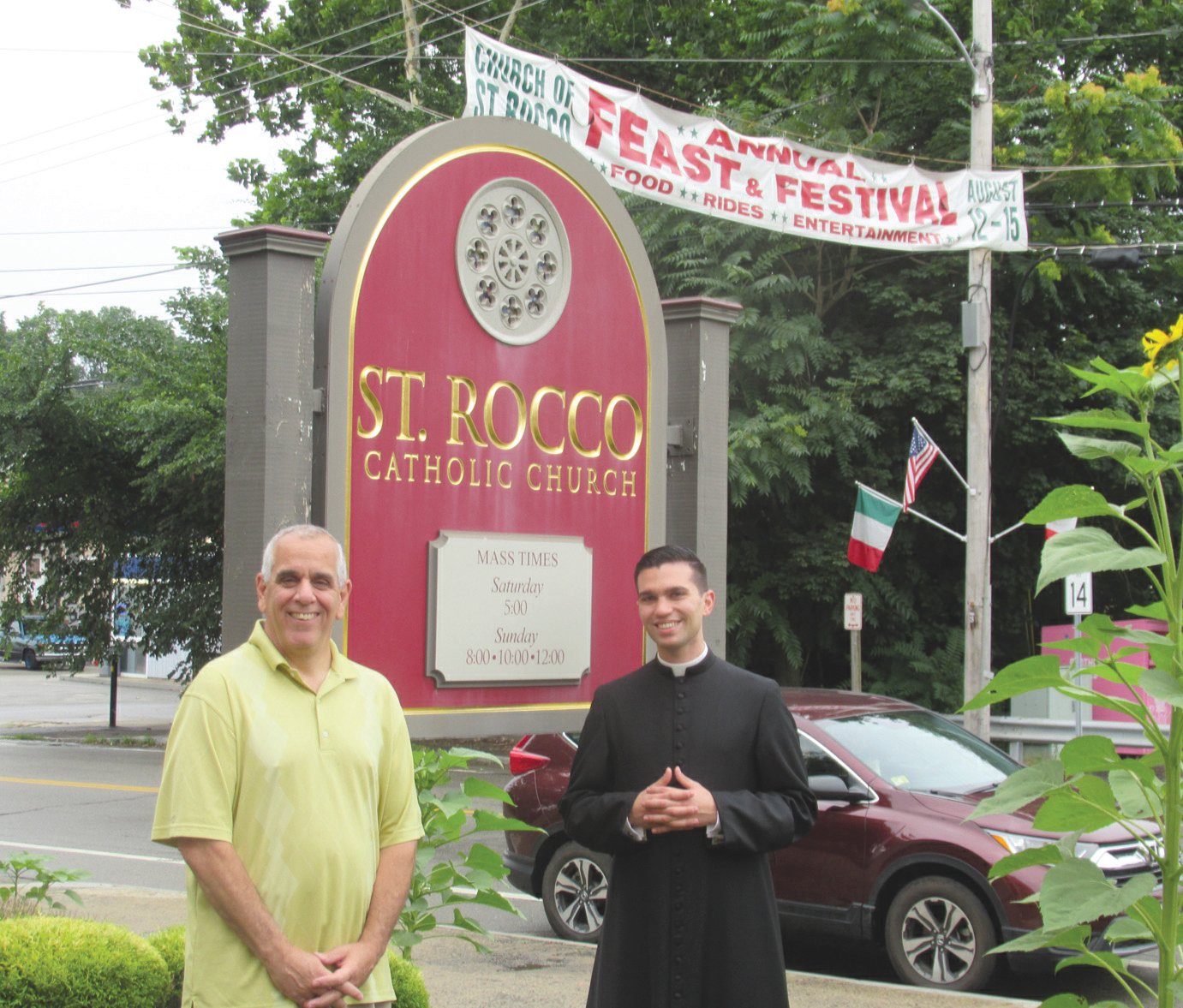 DIVINE DUTY: Richard Montella, left, long-serving co-chairman of the now 81-year-old Saint Rocco’s Feast and Festival, is joined by Seminarian Stephan Coutcher outside the Roman Catholic Church conveniently located on the corner of Plainfield Pike and Atwood Avenue in Johnston. (Sun Rise photos by Pete Fontaine) PIX TWO IMG 4178